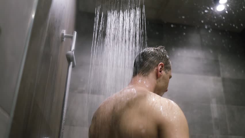 Caucasian man in shower washing hair showering in bathroom.  Young man rinsing shampoo and conditioner from hair in warm bath with modern bathroom.