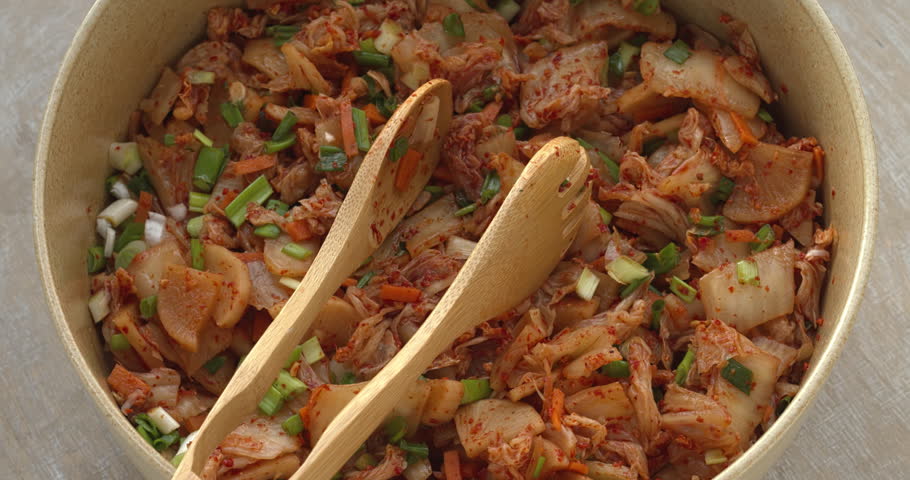 Homemade kimchi, a traditional Korean side dish of salted and fermented vegetables with garlic, ginger, and gochugaru in a big bowl with serving tongs. Table spin.