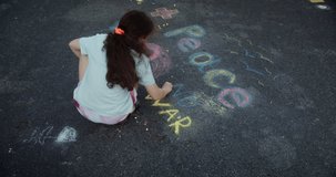 Cute little girl draw a peace on the asphalt with chalk .Video in 4K. Top view of little girl writing peace with chalk. Protest against war, Russian invasion of Ukraine.