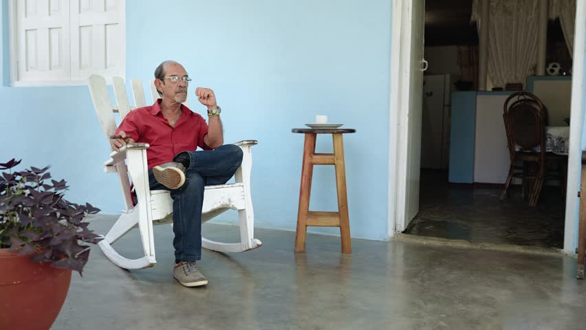 Senior Hispanic Man relaxing at home porch looking away - Retired Latin American Grandfather