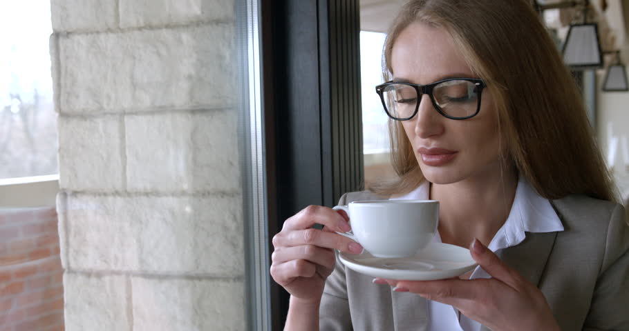 Attractive blonde businesswoman with glasses is enjoying her coffee in the cafe. Close-up indoor portrait.