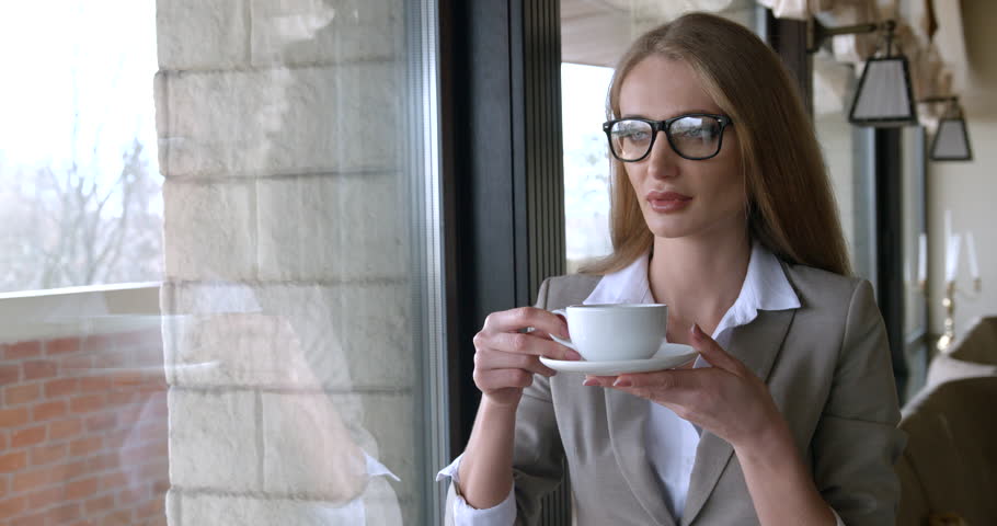 Close-up portrait of the young beautiful blonde businesswoman with glasses enjoying her tea in the cafe.