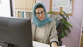 Smiling woman in hijab using smartphone for video call in modern office.