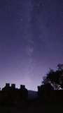 old castle in the night. Timelapse of moving star trails in night sky. A view of the stars of the Milky Way with a mountain top in the foreground. Perseid Meteor Shower observation. vertical video.