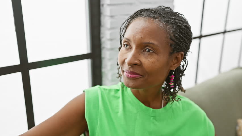 Smiling african woman in green top enjoys leisure time in brightly lit living room.