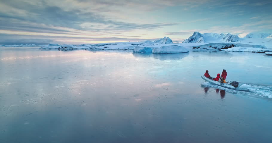 Tourists people sail on boat in Antarctica. Zodiac boat gently glides on waters surface in sunset light. Antarctica travel and exploration. Discover the beauty of South Pole. Aerial winter landscape