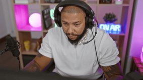 Focused black man with beard wearing headphones in a colorful gaming room at night, expressing concentration
