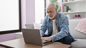 Mature bearded man in a denim jacket using a laptop comfortably in a well-lit living room. - Powered by Shutterstock - Get 15% off with code: PIKWIZARD15