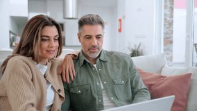 Happy middle aged couple using laptop relaxing on couch at home. Smiling mature man and woman looking at computer watching video, browsing or shopping in ecommerce store sitting on sofa in living room - Powered by Shutterstock - Get 15% off with code: PIKWIZARD15