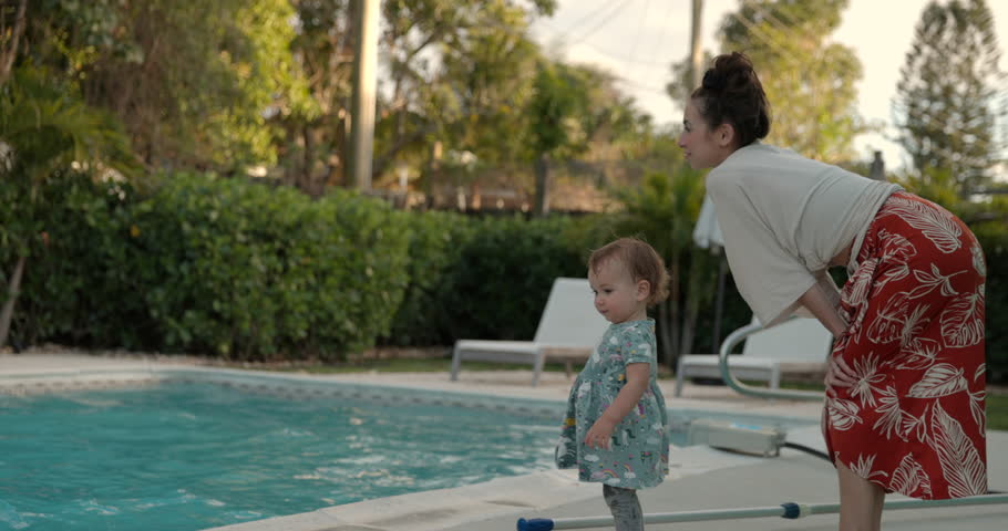 Toddler girl runs away from mother outdoors by family swimming pool