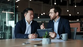 Two multiracial business colleagues looking at digital gadget screen and talking about data on display. Concentrated men in jacket watching on company stock price and debating reasons of chart growth. - Powered by Shutterstock - Get 15% off with code: PIKWIZARD15