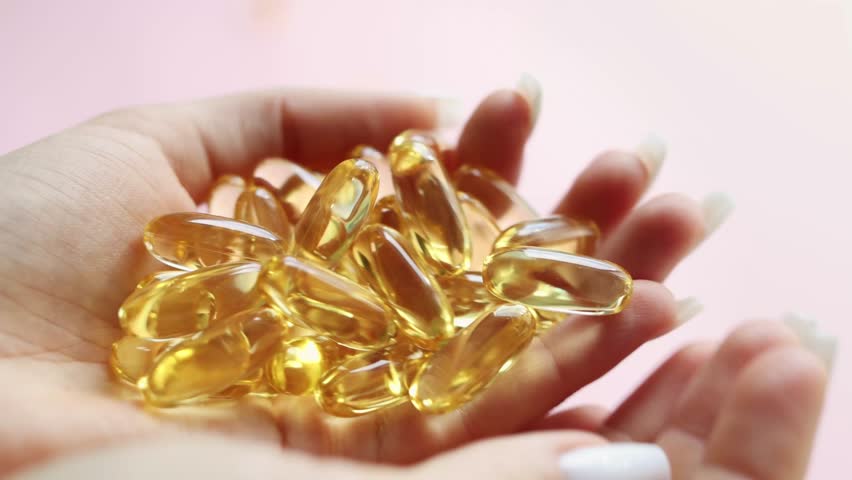 Close-up medicine yellow transparent pills, omega 3 fish oil capsules, vitamin D. A young woman pours yellow transparent capsules from hand to hand. The concept of health, vitamins, and medicine