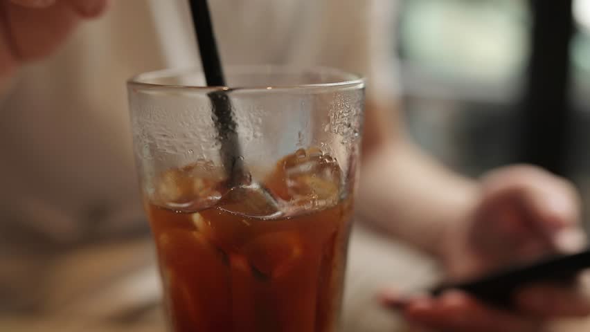 A close-up of a man, in a summer morning cafe, stirring an espresso with one hand, while using a phone with the other.