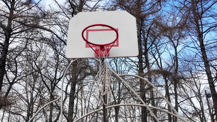 Outdoor basketball basket with torn net wobbly in the wind
