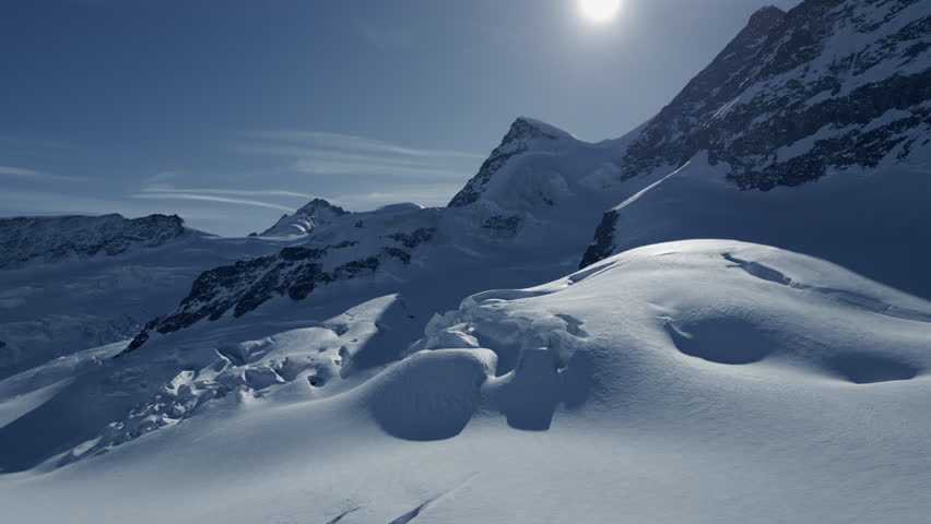 Sunlight breaks through clouds, illuminating snowy mountain slopes