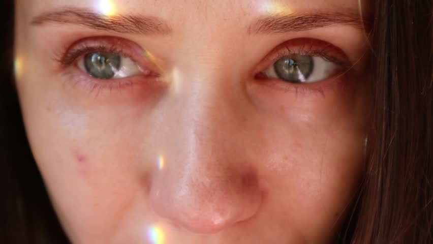 Young attractive woman with beautiful green blue eyes and glare of light on her face looking away. Female portrait with sunny beams, rainbow rays.