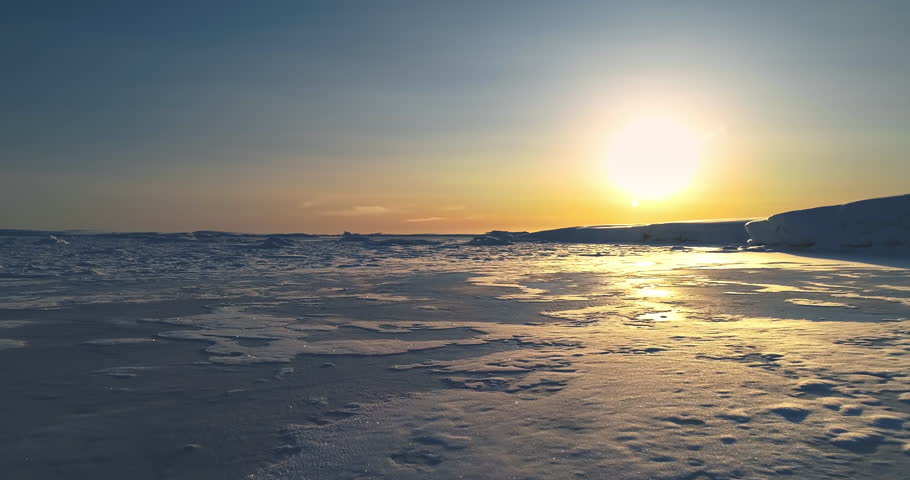 Fly over sunset frozen ocean in Antarctica. Sun warm glow reflect on icy surface. Antarctica travel background and exploration. Discover the beauty of South Pole. Desert white land of snow drone shot.