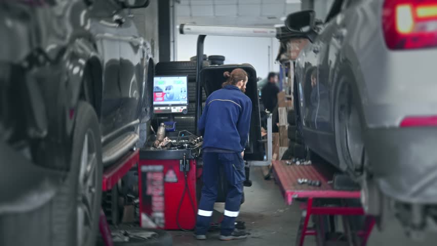 Technician work car service. Auto mechanic balancing big wheel. 30s man change tyre cover job. Guy fix tire workshop. Worker repair vehicle. Repairman person replace cast disk. Engineer blue uniform.