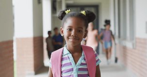 Video of happy african american girl standing at school corridor. primary school education and learning concept.