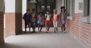 Video of happy diverse pupils running on school corridor. primary school education and learning concept.