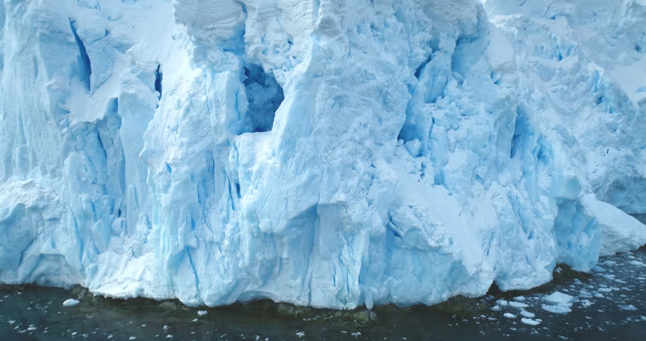 Giant glacier towering in Antarctica polar ocean. A huge iceberg ice wall formation float cold water, mountain slope in background. Winter landscape close up. Climate change at polar glacier landscape