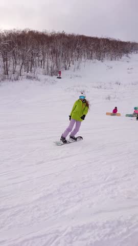 Cheerful snowboarding girl in green jacket skiing down the hill