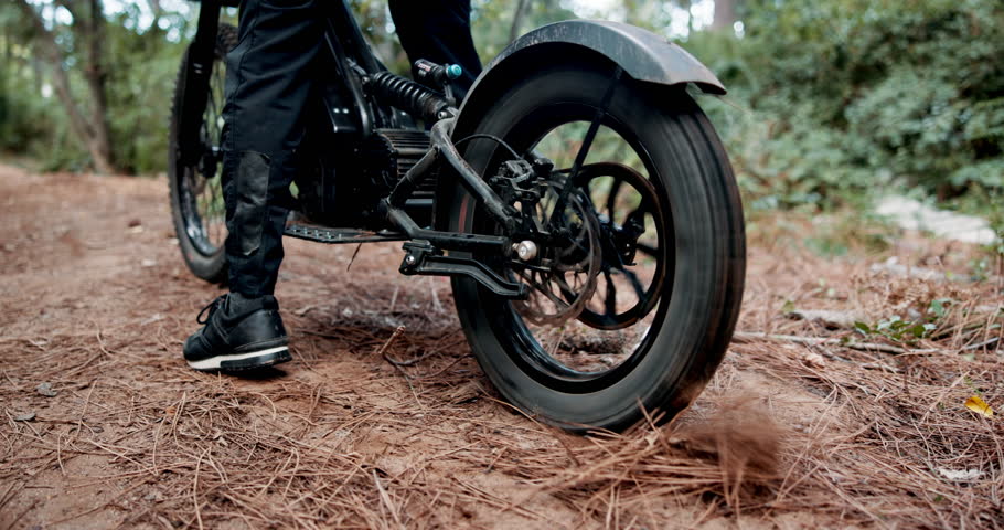Person, dirt bike and feet on forest trail with tyre spin, speed and start with dust for adventure. Motorcycle, rider and ready for race, transportation or journey with shoes on ground path in woods