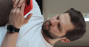 Vertical video: Young man call on phone closeup, use loudspeaker at home. Man recording answering by audio message in social network on mobile phone.