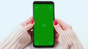 Woman with red nails using green screen chroma key smartphone in vertical position close up on white background. Female person holding phone