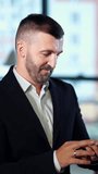 Businessman standing in office and holding phone. Entrepreneur messaging to somebody. Portrait close up. Females in blur at backdrop. Vertical video