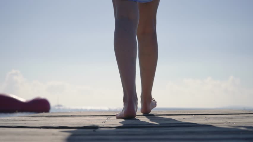 A woman in hat and shirt walks over a wooden pier and seat on edge in the tropical island, slow motion