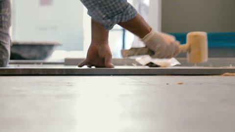 Cinemagraph of worker putting ceramist tile on the floor. He presses the tile to the floor with a wooden hammer.