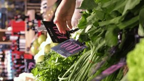 Vertical video. Close-up of female buying green vegetables at grocery, choosing between long beans, garlic chives and parsley