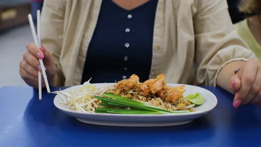 Young woman eating Pad Thai (Stir-Fried Noodles) with shrimps indoors. Traditional Thai food concept