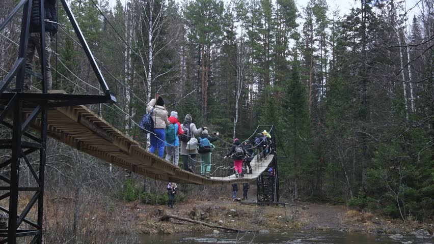 a group of people walking on a suspension bridge in the autumn