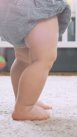 Baby learning to walk taking first steps at home. Little feet walking on floor at living room