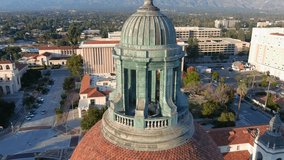 backwards aerial footage of the bell tower at city hall with office buildings, shops and apartments in the city skyline in Pasadena California USA