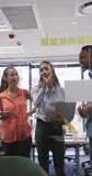 Vertical video of diverse business people taking notes on glass wall in office. global business in creative office and body inclusivity.