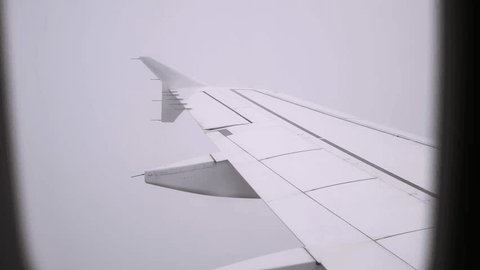 View on an airplane wing in clouds through a porthole. Cloudy sky background. A passenger plane flying in fog. Bad weather and visibility. Concept of people's fear traveling by air. Aerophobia. 4K. Adlı Stok Video