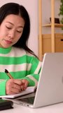 Vertical screen video. Young smiling freelancer asian woman using calculator working on laptop computer at home.