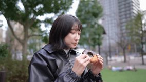 Slow motion video of a Japanese woman in her 20s eating donuts in a park around Gotanda Station in Shinagawa-ku, Tokyo in winter