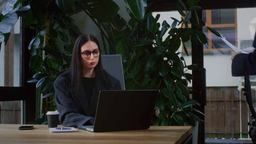 Two girls in a office discuss documents or a project on paper. Teamwork in coworking. Businesswomen in glasses create a marketing plan. Caucasian female people are working on a laptop. Modern office Royalty-Free Stock Footage #3475048593