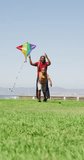 Vertical video of happy african american father with son flying kite. spending free time during holiday.