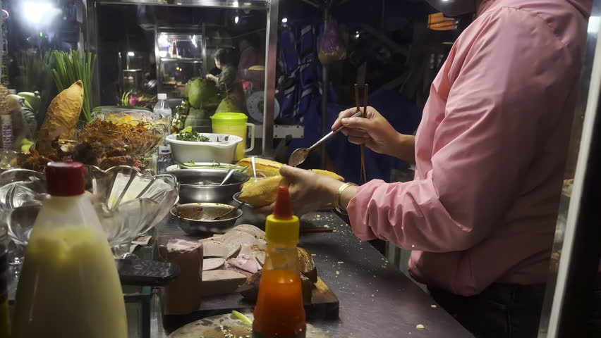 Vietnamese women preparing Banh Mi Sandwind with chopsticks. Banh mi cart where women are making tourists Ban Mi sandwiches in Hoi An, Vietnam. Royalty-Free Stock Footage #3475141753