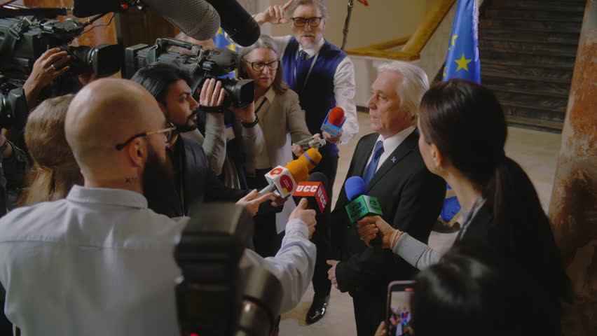 EU representative answers press questions and gives interview for TV breaking news. Senior consul surrounded by crowd of journalists. Political speech during press conference. State of the nation.