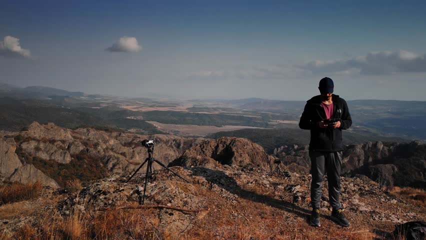 Man stands on the rocky mountains of Birtvisi in Georgia and pilots drone with remote control in his hand. Photographer captures amazing scenery o Caucasus cliffs during his active weekend on trekking