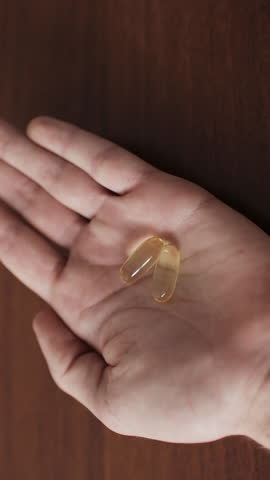 Man shaking food supplements into hand. Yellow softgel capsules Omega-3. Vertical video.