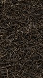 Close-up view of Chinese raw maturing (mao cha) green Pu Erh dried tea leaves as an abstract food background. Spin around center point. Vertical video.