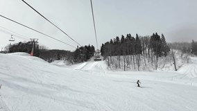 Ski vacation holidays getaway concept. White snowing weather with ski lift in winter landscape with snow and trees, mountain. Beautiful cold day at ski resort with ski chair lift. Low light Video 4K.