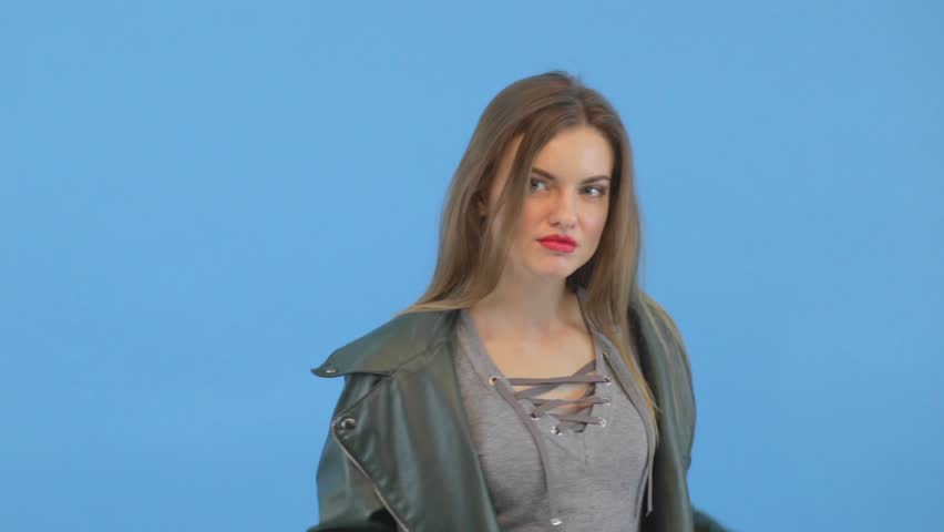 Beauty young hot girl in leather jacket poses by the camera. Seductive look, stylish wear. Blue background. Natural beauty footage